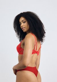 Red lace bra featuring adjustable straps and a back closure, paired with a matching red thong. Smooth, stretchy fabric with detailed lace.