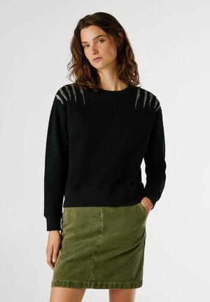 Felpa nera con dettagli metallici argento sulle spalle, con colletto rotondo e maniche lunghe, abbinata a una gonna in velluto a coste verde.