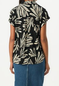Czarna koszula z krótkim rękawem w liściasty beżowy wzór, z plisą z tyłu i luźnym krojem, połączona z dżinsową spódnicą.