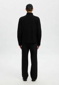 Svart fleecejacka med hög krage, detaljerad sömnad och lös passform, ihop med svarta vida byxor och svarta skor.