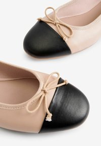 Beige bőrből készült balerina cipők fekete bőrfedő orral, apró masnival és rugalmas szélekkel a kényelmes illeszkedés érdekében.
