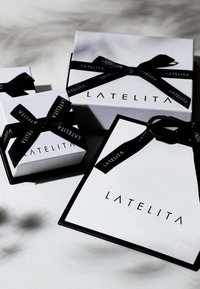 Kolme valkoista lahjarasiaa mustalla nauhalla, joissa on "LATELITA"-brändäys. Rakenteellinen paperi ja erottuvat muodot, jotka vaihtelevat pienestä suureen.