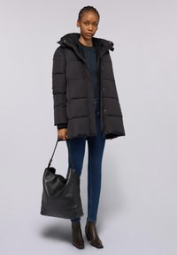 Svart puffjacka med huva, med dragkedja och horisontell sömnad. Matchad med mörka jeans och en svart läder tote-väskan.