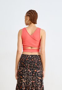 Różowy prążkowany top w stylu crop z krzyżującymi się plecami, zestawiony z zwiewną czarną spódnicą w kwiaty z czerwono-pomarańczowymi wzorami.