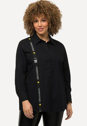 Camicia nera a bottoni con una vestibilità comoda, caratterizzata da una fascia decorativa con testo e stelle gialle lungo il lato. Tessuto dalla texture liscia.