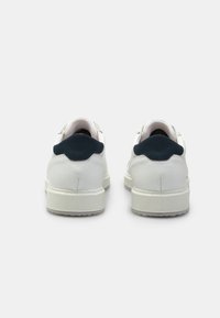 Sneakers bianchi in pelle con tacco in suede blu scuro. Presentano una texture liscia, una forma arrotondata e una suola in gomma. Design minimalista.