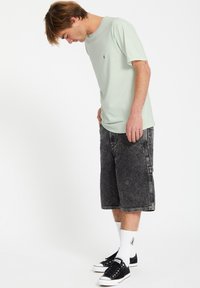 Lys grøn bomulds t-shirt med korte ærmer, parret med sorte denim shorts. Sorte sneakers med hvide detaljer og hvide sokker er båret.