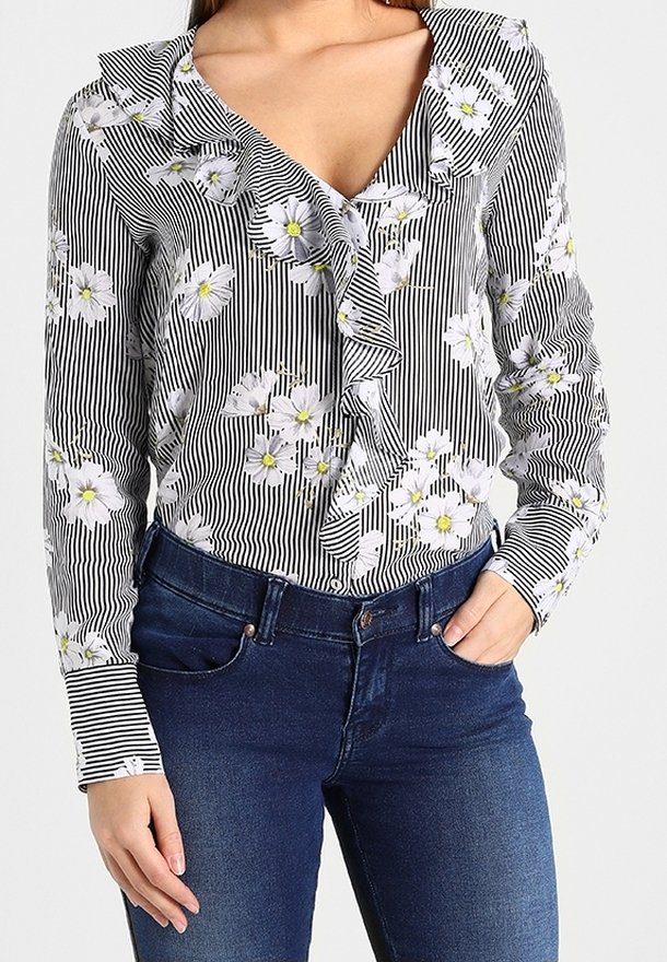 Svartvit randig blus med vita blommönster, volangkrage, långa ärmar och knäppning fram. Bärs med blå jeans.