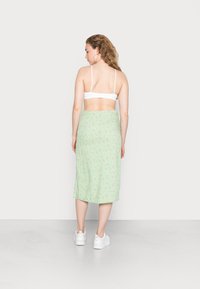 Saia midi verde com flores pequenas rosas, textura suave e um cós ajustado. Usada com ténis brancos e um bralette branco.