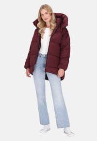 Jachetă puffer de culoare burgundă, cu o glugă mare, închidere cu fermoar și model matlasat, asortată cu blugi evazați de culoare bleu deschis și adidași albi.