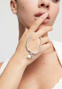 Bracelet perlé en argent avec un centre lisse et incurvé et deux breloques : une petite perle blanche et un fer à cheval détaillé.