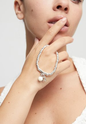 Pulsera de cuentas plateadas con un centro liso y curvado y dos dijes: una pequeña cuenta blanca y una herradura detallada.