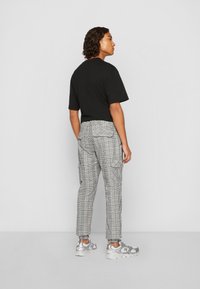 Schwarzes kurzärmeliges T-Shirt kombiniert mit grauen karierte Cargo-Hosen mit Taschen. Das Modell trägt silberne Sportschuhe. Sanfter Hintergrund.