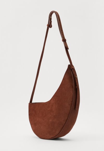 Sac à épaule en daim marron avec une forme courbée, une bandoulière ajustable et un design minimaliste. Texture lisse sans matériel ou accents visibles.