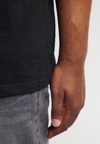 Camisa negra de manga corta con una superficie texturizada, combinada con pantalones grises. Presenta un corte casual y detalles de costura visibles.