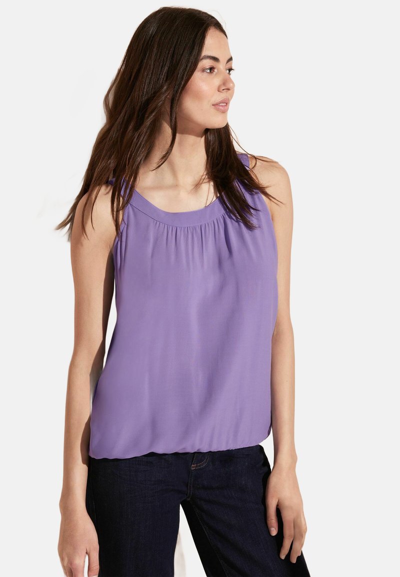 Top morado sin mangas con escote redondeado y detalles fruncidos, combinado con jeans de mezclilla oscuros. Tela suave con una textura lisa.