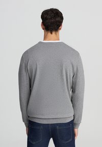 Felpa grigia con maniche lunghe, colletto a girocollo a coste e polsini a coste. Tessuto morbido con una vestibilità comoda, abbinata a jeans blu scuro.