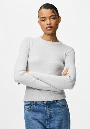 Jasnoszary sweter w prążki z długimi rękawami i okrągłym dekoltem. Charakteryzuje się dopasowanym krojem i fakturowanym materiałem. W zestawie z niebieskimi dżinsami.