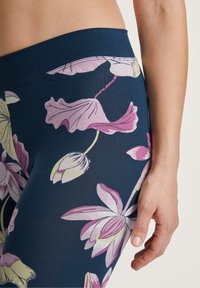 Ingrandimento dell'anca e del braccio di una persona che indossa leggings blu navy con stampa floreale rosa e gialla e una cintura larga.