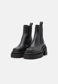 Czarne skórzane botki za kostkę z elastycznymi bocznymi panelami, masywnymi podeszwami platformowymi i teksturowanym wzorem na bieżniku. Posiadają uchwyt z tyłu.