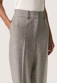 Grå højderede bukser med subtilt tekstureret stof, for-pleats, sidelommer og bæltestropper, præsenteret mod en neutral baggrund.