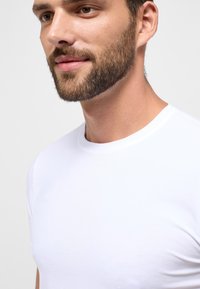 Hvid T-shirt med korte ærmer lavet af glat bomuldsstof, med en klassisk rund hals; teksturen ser blød og behagelig ud.