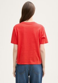 Rode katoenen T-shirt met korte mouwen en een ronde hals, met een relaxte pasvorm en een rechte zoom, gecombineerd met blauwe spijkerbroek. Achteraanzicht.