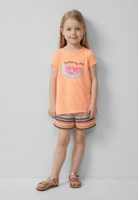 Kinderen oranje T-shirt met de tekst "Sweeter my day" en een paillettengebed van een watermeloen, gecombineerd met meerkleurige gestreepte shorts en sandalen.