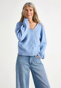 Cardigan bleu deschis cu decolteu în V, închidere cu nasturi, manșete și tiv rebiți. Asortat cu blugi evazați din denim. Textură moale.