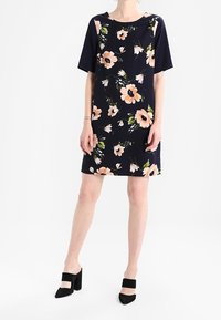 Květinové šaty s krátkým rukávem v námořnické modři se broskvovými a zelenými květy, s rovnýřezem a lehkým materiálem. Černé boty na blokovém podpatku.
