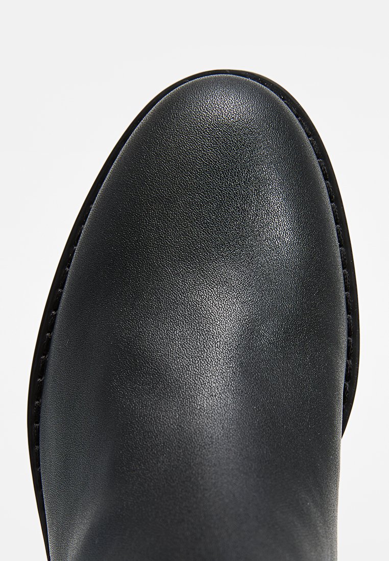 Botte en cuir noir jusqu'à la cheville avec un bout arrondi, texture lisse et un accent de couture minimal le long de la semelle.