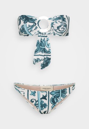 To-delt bikini sett med en bandeau-overdel med en sirkulær detalj og en knytning. Stoffet har et blått blomsterdesign på en hvit bakgrunn.