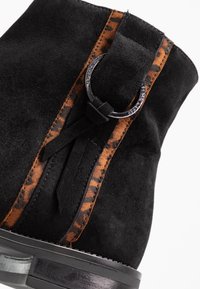 Bottine en daim noir avec un panneau imprimé léopard marron, une bride en cuir avec une boucle métallique circulaire, et une semelle texturée.