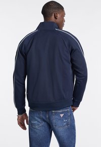 Tumši zila sudraba ar stāvu apkakli, ar baltām svītrām uz piedurknēm un ribinātu apakšmalu. Saskaņota ar gaiši ziliem nolietotiem džinsiem.