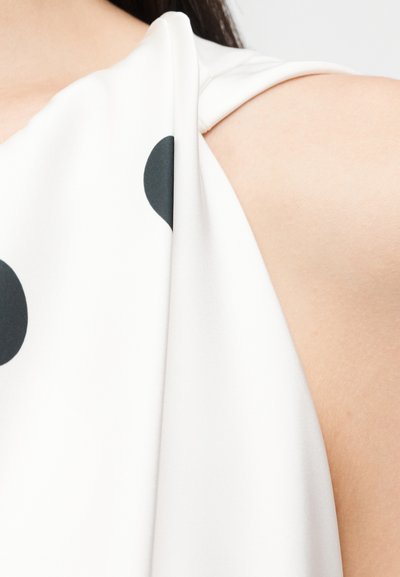 Κοντινό πλάνο ενός λευκού αμάνικου τοπ με μεγάλα μαύρα πουά που φοριέται στον ώμο ενός ατόμου.