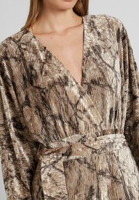 Vestido largo de estilo envolvente, hecho de una tela texturizada y estampada en tonos marrón y crema. Presenta un escote en V profundo y una cintura atada.
