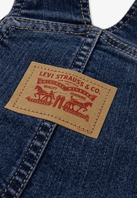 Salopette en denim avec une étiquette en cuir marron arborant du texte rouge et des images, affichant la marque Levi Strauss & Co. et des détails de brevet.