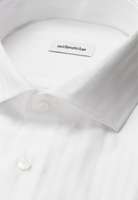 Camicia bianca con sottili strisce verticali, colletto button-down e un solo bottone sul collo. L'etichetta riporta "seidensticker."