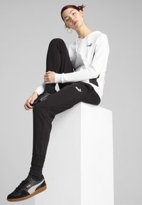 Vit zip-hoodie och svarta joggers i mjukt tyg, tillsammans med svarta och grå sneakers. Outfiten har en Puma-logotypdetalj.