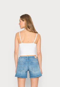 Top cropped branco em algodão com alças ajustáveis finas, emparelhado com calções de ganga azul claro com bolsos traseiros e um design costurado.