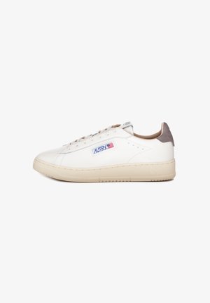 Sneaker in pelle bianca con suola in gomma beige, punta rotonda, cuciture sottili e accentuazione in suede grigia sul tallone. Logo laterale in blu e rosso.