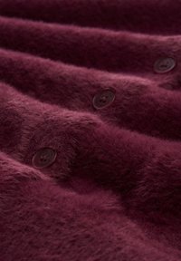Bordeauxkleurige textiel met een zachte, fuzzy uitstraling, voorzien van donkere knopen die in het materiaal zijn genaaid.