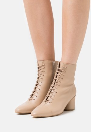 Beige lace-up ankle boots with side zipper and block heels worn on bare legs against a white background.