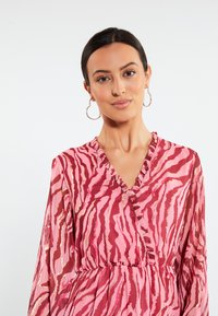 Rochie roz cu dungi zebra în nuanțe de roz și roșu, având un decolteu în V și detalii cu volane pe față. Material mătăsos.