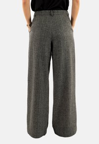 Wijdvallende broek van grijze tweed stof. Heeft een hoge taille, steekzakken en een gladde textuur met subtiele patronen.