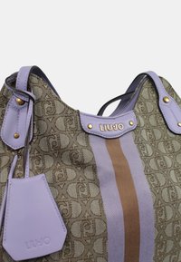 Borsa a tracolla in tessuto marrone a fantasia con rifiniture sintetiche viola e striscia marrone, dotata di accessori in oro e un piccolo etichetta viola con logo.