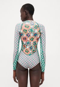 Langermet badedrakt med blomster- og geometriske mønstre i pastellfarger. Laget av elastisk stoff med kontrastsøm og en tettsittende design.