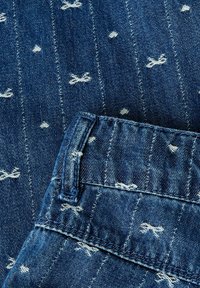 Tumesinine denim kangas, millel on valged õmblusmustrid, mis meenutavad kaari. Omab kaarduvat vöökohta, mille servad on purustatud. Tekstuuriga ja vastupidav.