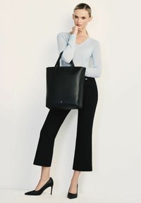 Czarna skórzana torba z dwoma uchwytami na górze, w pionowym kształcie, o gładkiej fakturze, w połączeniu z jasnoniebieskim swetrem i czarnymi spodniami typu cropped.