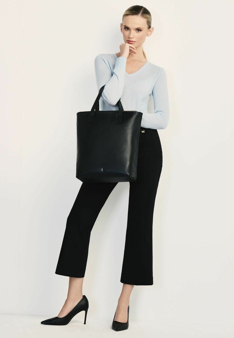 Czarna skórzana torba z dwoma uchwytami na górze, w pionowym kształcie, o gładkiej fakturze, w połączeniu z jasnoniebieskim swetrem i czarnymi spodniami typu cropped.